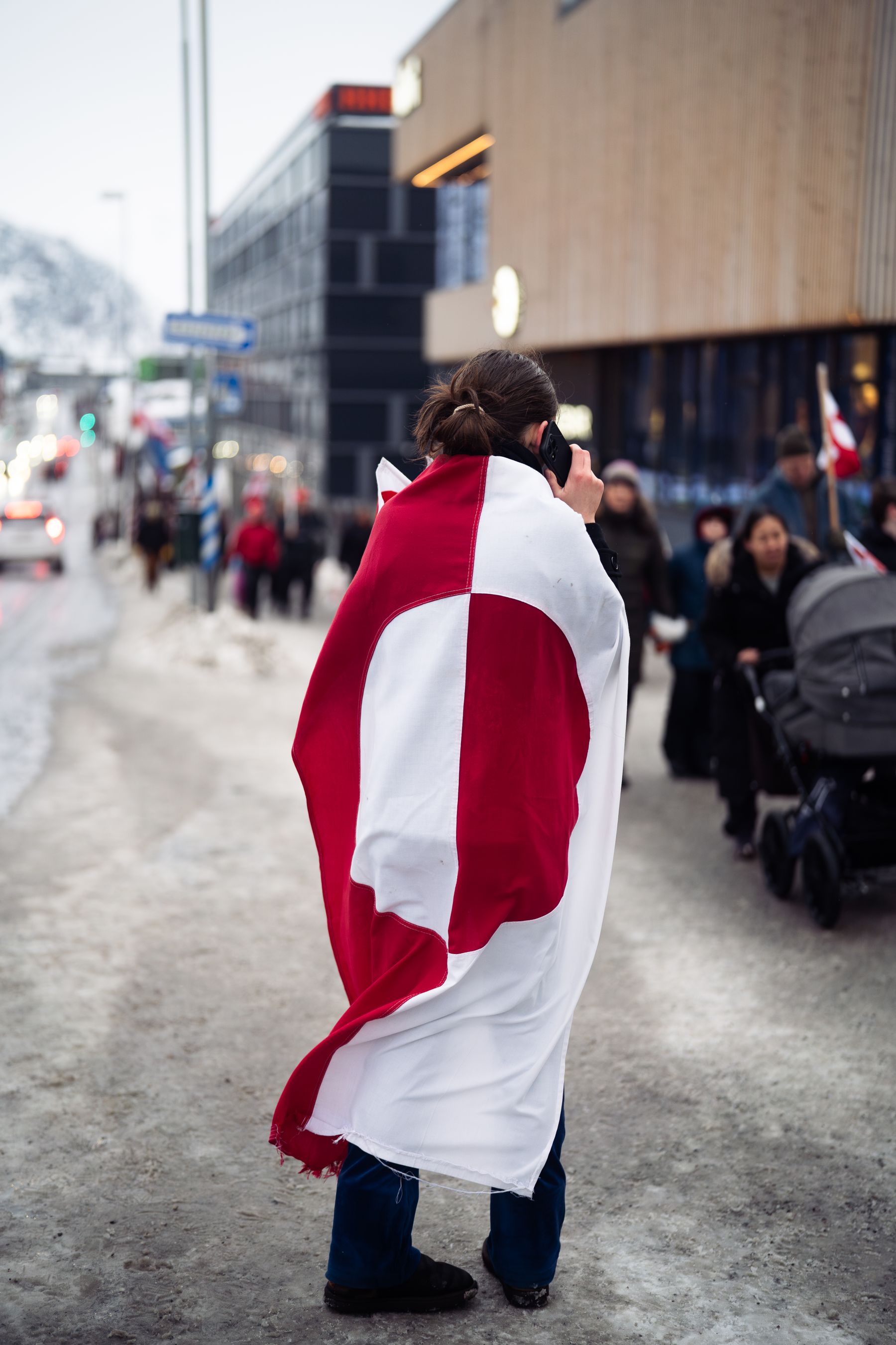 Person svøbt i Grønlands flag på en sneklædt gade i Nuuk